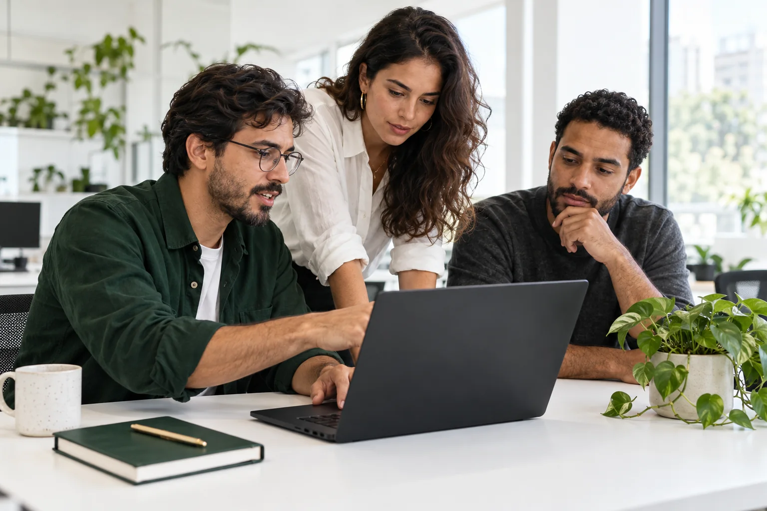 Pessoas colaborando com um notebook em um ambiente claro; uma delas veste verde-floresta